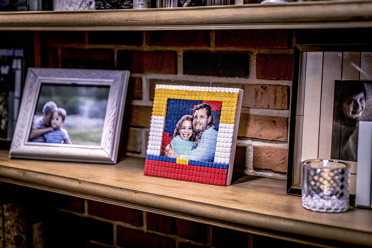 Ein personalisiertes LEGO Mosaik-Bild auf einem Regal, umgeben von Familienfotos. LEGO Mosaik-Bild personalisiert